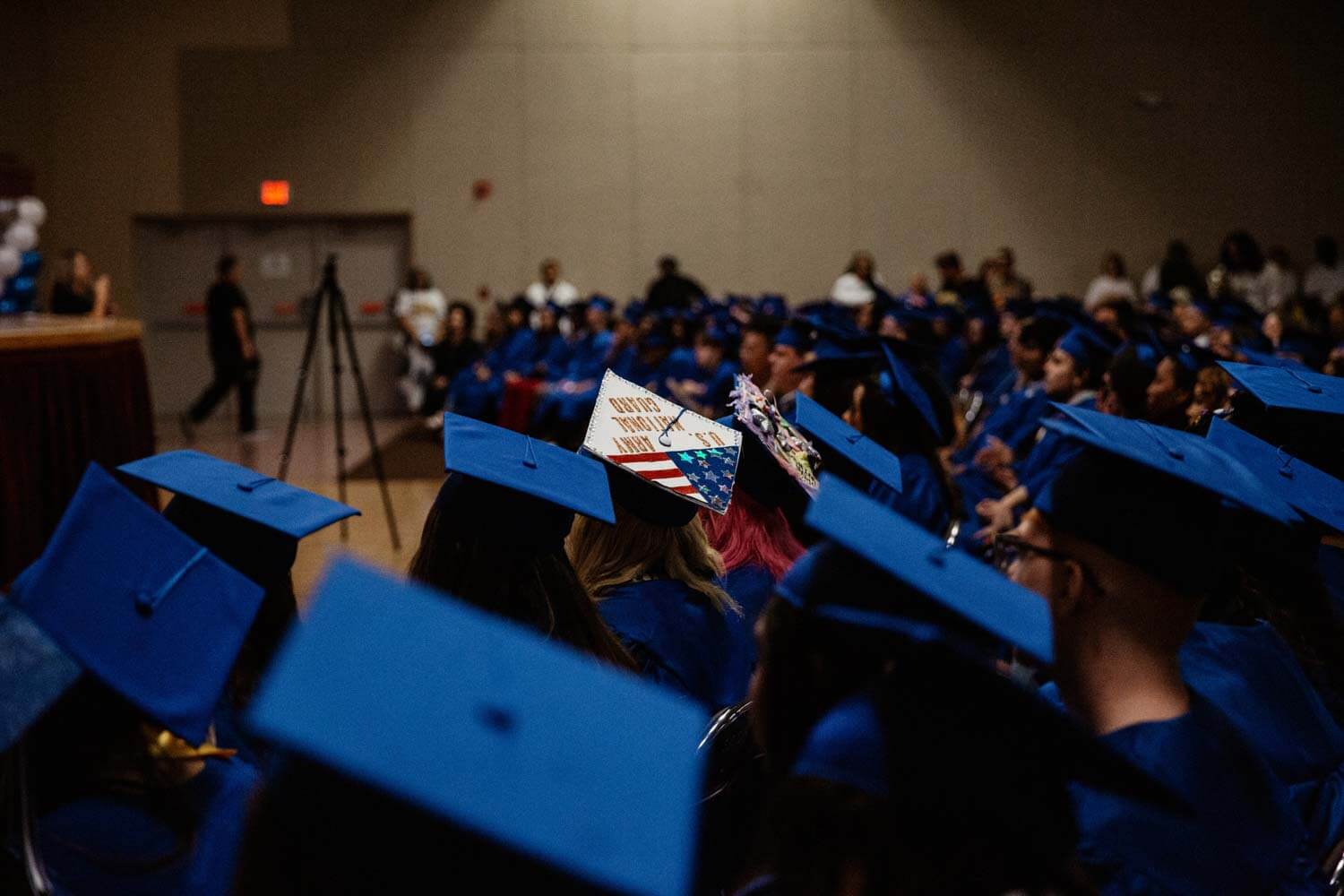 Graduates in blue caps and gowns sit in rows.