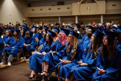 Graduates in blue caps and gowns seated in rows at a ceremony, conveying excitement and anticipation.