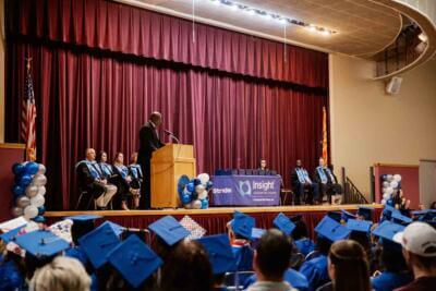 Graduation ceremony with students in blue caps and gowns facing a stage.