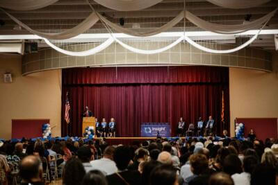 A graduation ceremony in a decorated auditorium featuring a speaker at a podium.
