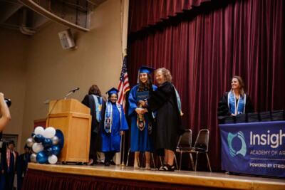 Graduation ceremony with a smiling graduate in blue robes receiving a diploma on stage.